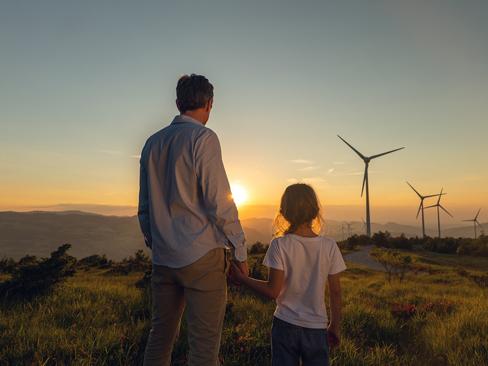 Vater und Tochter schauen auf Windpark im Sonnenuntergang